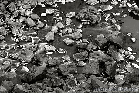 Fine art black and white photograph of grey, white and black rocks at the bottom of a river canyon