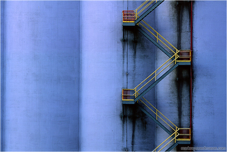 Silo, Stairs: Vancouver, BC, Canada (2004-00-00) - Abstract photograph showing a yellow fire escape winding down a huge grain silo