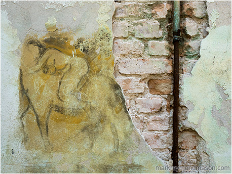 Fine art photograph of a charcoal mural on a chipped and stained concrete wall, with bricks and pipes exposed beneath the damage