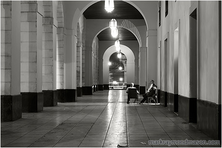 Fine art black and white photograph showing several bank guards lounging in chairs in an empty breezeway