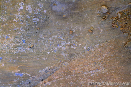 Fine art photograph of red stones cascading like water down a sandstone slope, surrounded by blue tinted lichen