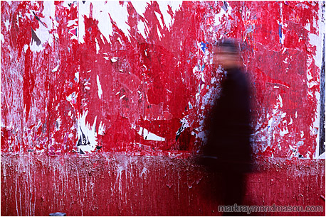 Abstract photo of a red wall and a blurry walking man with an accusing stare