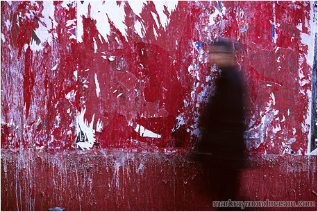 Abstract photo of a red wall and a blurry walking man with an accusing stare