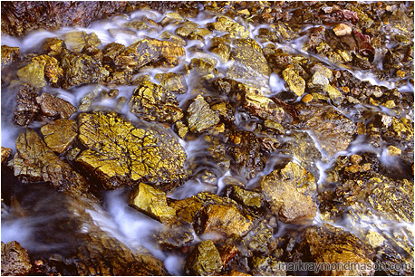 Fine art abstract photograph of an alpine stream flowing around broken yellowed limestone blocks