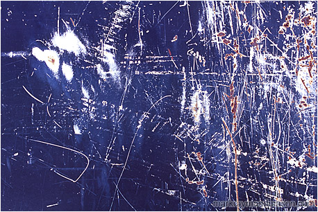 Abstract photograph of chaotic white and rusty scratches on the surface of a dark blue painted piece of scrap metal