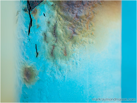Abstract macro photograph showing bubbling rusted paint between blue and amber highlights