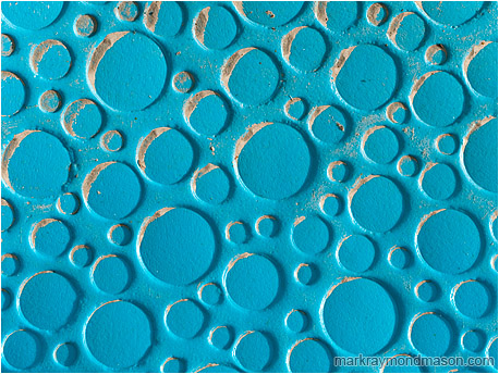 Abstract photograph showing an array of blue plastic circles, some partly filled with drifting sand