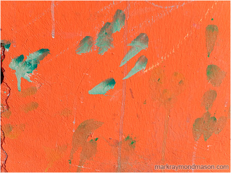 Abstract urban photograph showing smudges of grey paint on a crumbling orange concrete wall