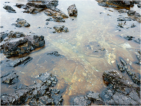 Fine art photograph of sharp black rocks scattered around a colourful tide pool