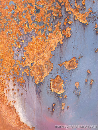 Abstract photograph of swirled red rust on the surface of a bluish painted metal plate
