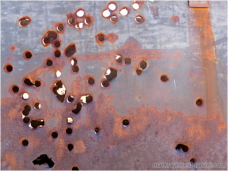 Fine art photograph of bullet holes through a rusted metal plate wall