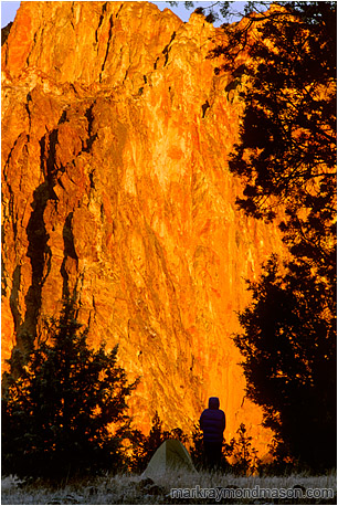 Lifestyle photo of a silhouetted woman and her tent, in front of a wall of bright orange, sunlit rock