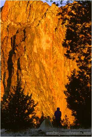 Lifestyle photo of a silhouetted woman and her tent, in front of a wall of bright orange, sunlit rock