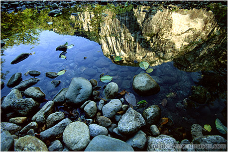 Abstract photograph showing reflections of cliffs and river rocks in calm water