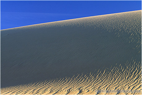 Abstract nature photograph of shadows in a sand dune and pale blue sky