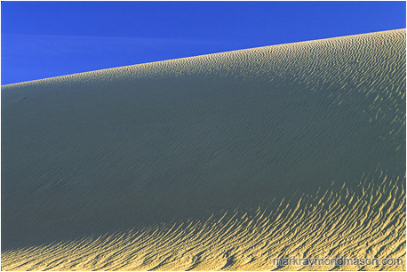 Abstract nature photograph of shadows in a sand dune and pale blue sky