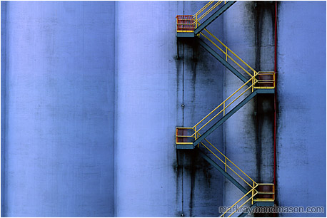 Abstract photograph showing a yellow fire escape winding down a huge grain silo