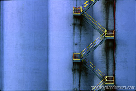 Abstract photograph showing a yellow fire escape winding down a huge grain silo