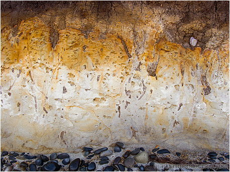 Fine art photograph of orange and red patina over a compact mud seaside cliff