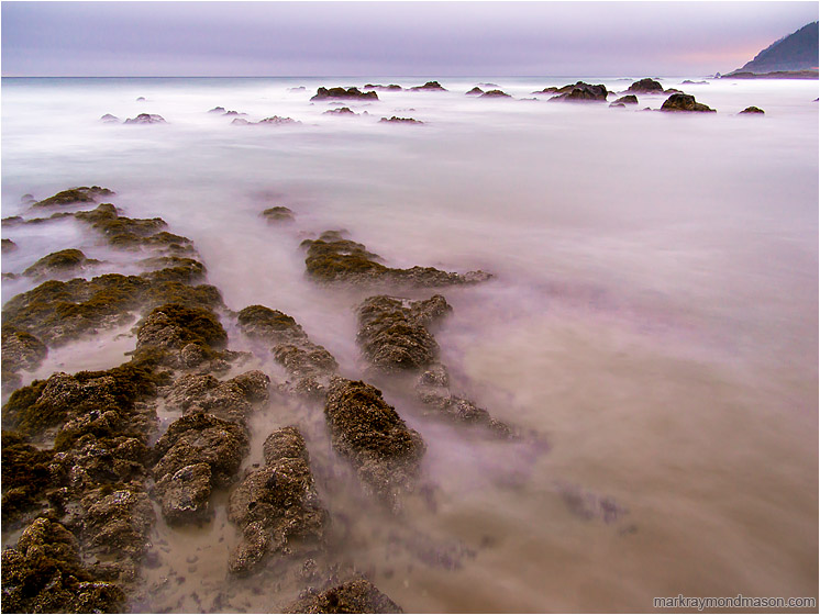 Calloused Stones, Murky Sea: Near Stawberry Hill Park, OR, USA (2015-10-21) - Fine art long-exposure photograph of barnacled rocks and clouds of sand as seawater washes over a tidepool