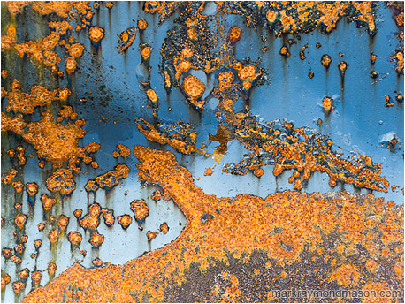 Abstract fine art photograph of red rusted spots looking like islands in an sky-blue sea of paint