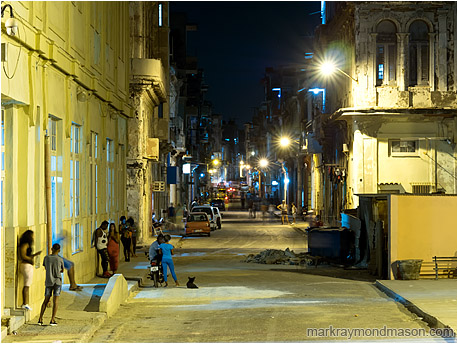 Fine art photograph showing a night time street scene in downtown Havana lit by garish street lamps