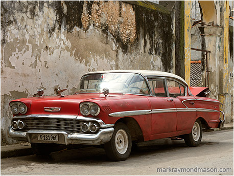 Fine art photograph of a dingy 1950s era car in soft light, in front of a checked and stained concrete wall