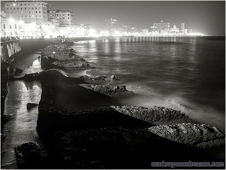 Fine art black and white night photograph of waves crashing against worn concrete water barriers