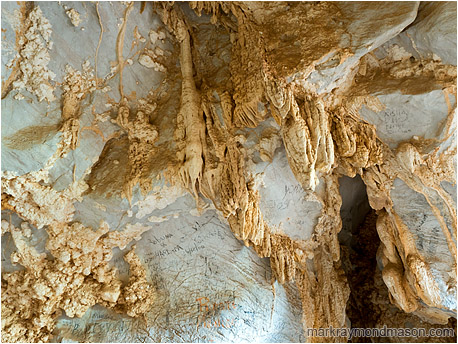Abstract photo showing popcorn rock and stalactites on the roof of a cave, with black charcoal graffiti all around